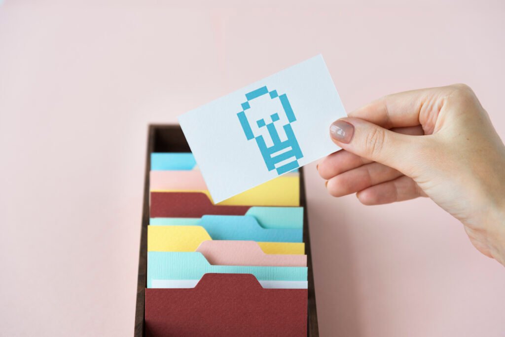 Una mano sostiene una tarjeta con un icono de teléfono frente a un archivador de colores.