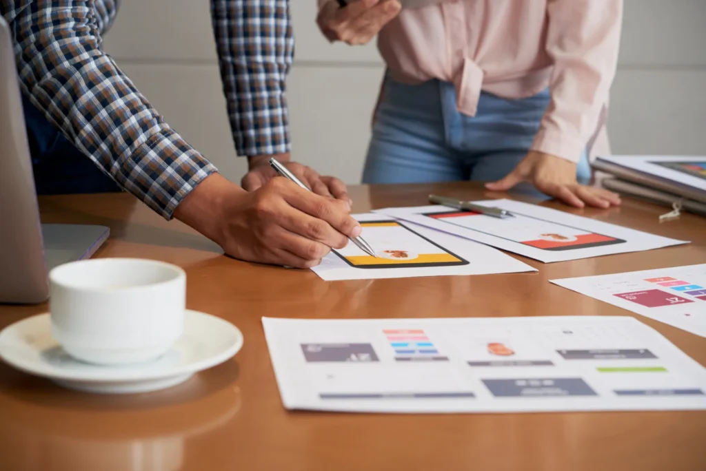 Dos personas revisan prototipos de pantallas sobre una mesa.