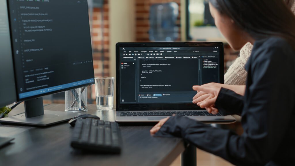 Dos desarrolladores señalan y revisan código en la pantalla de un portátil.